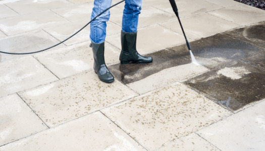 Someone standing on a patio using a pressure washer to clean pavers